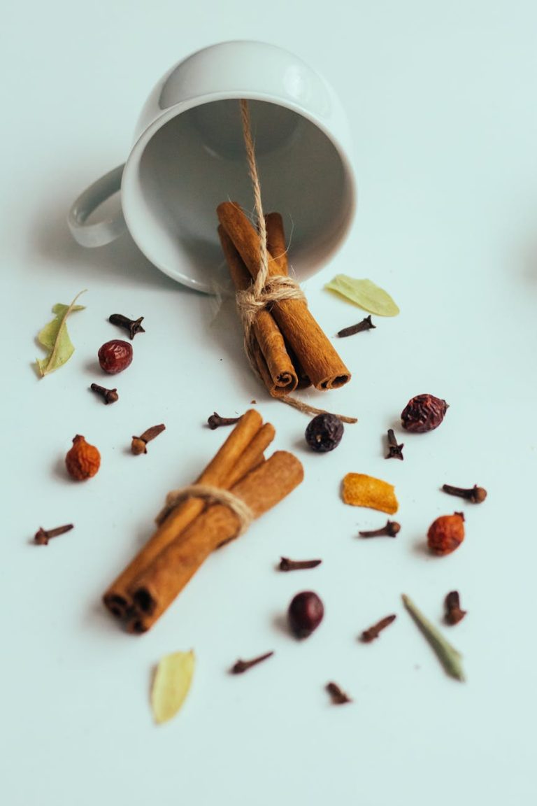 An artistic display of cinnamon sticks and spices spilling from a white cup.
