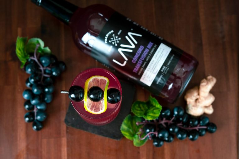 Top view of a refreshing cocktail with grapes, lemon, and ginger on a wooden table.