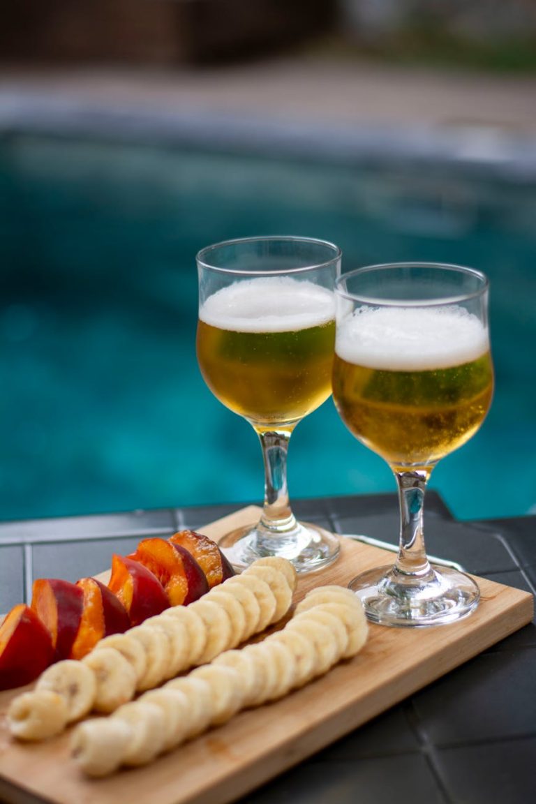 Two glasses of chilled beer and fresh fruit slices by a poolside, perfect for summer relaxation.