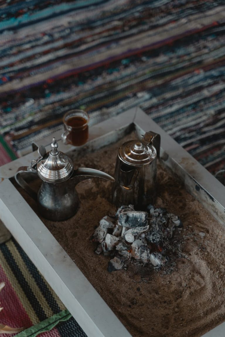 Silver teapots on sand heated by charcoal, traditional coffee brewing setup.