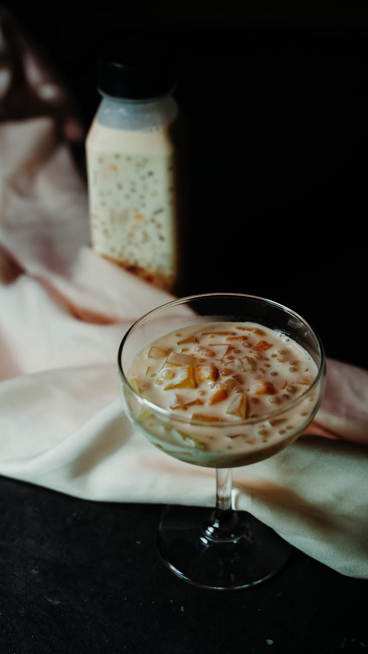 A delicate mango tapioca dessert served in a glass coupe with a bottle in the background.