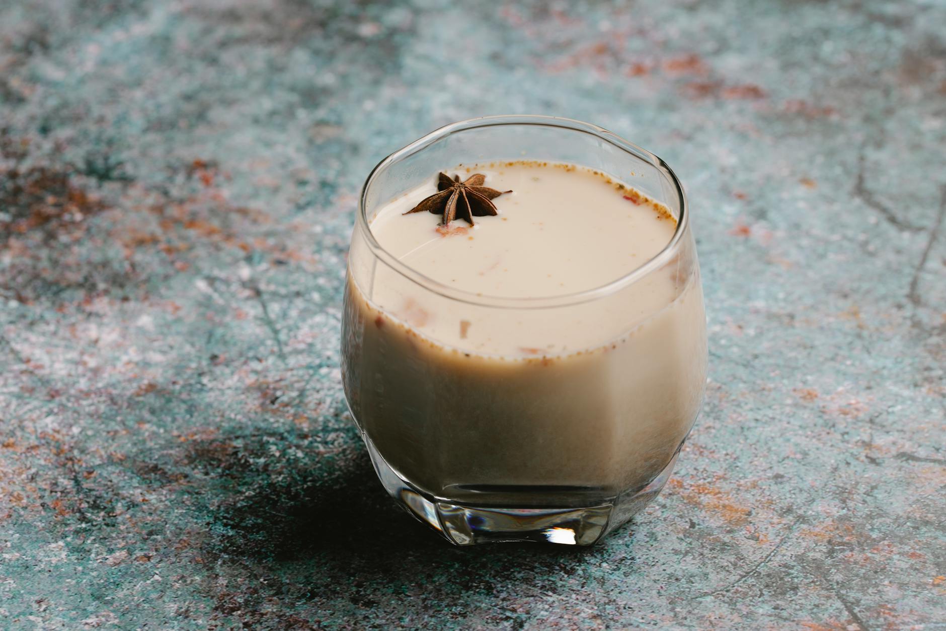 Aromatic chai latte in a glass with star anise garnish on rustic surface.