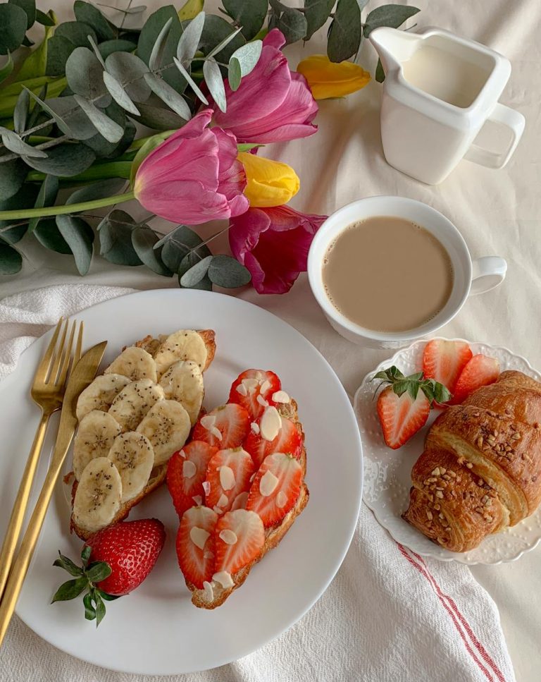 A cozy breakfast scene with toast, croissants, fresh fruit, coffee, and flowers.