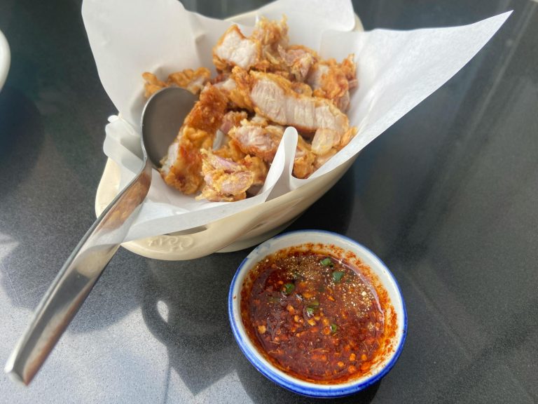 Plate of crispy Thai pork served with a spicy chili dipping sauce, perfect for a flavorful meal.