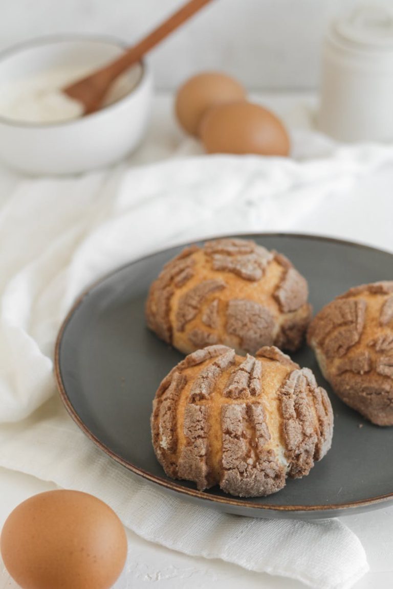 Close-up of sweet bread rolls on a plate with raw ingredients nearby, showcasing bakery essentials.