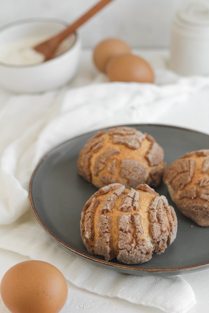Close-up of sweet bread rolls on a plate with raw ingredients nearby, showcasing bakery essentials.