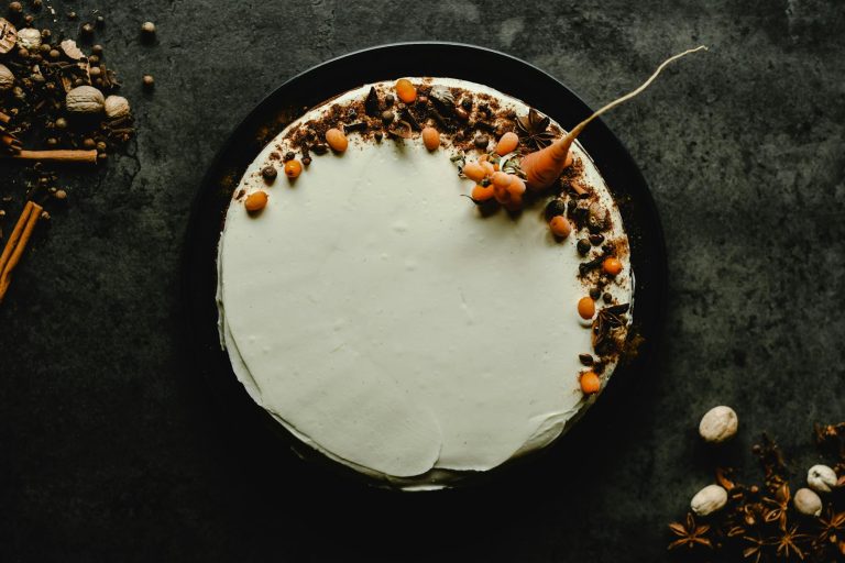 Top view of a carrot cake with cream cheese frosting garnished with spices on a dark textured background.