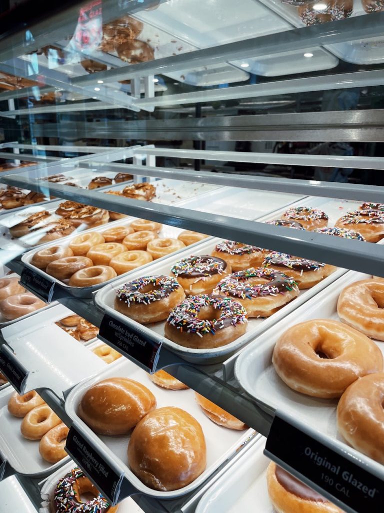Assorted donuts with sprinkles and glaze in a bakery display case, highlighting fresh selection.