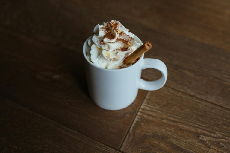 A delicious cinnamon latte topped with whipped cream served in a white mug on a wooden table.