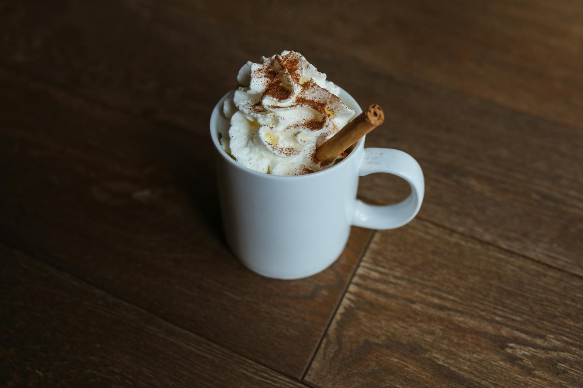 A delicious cinnamon latte topped with whipped cream served in a white mug on a wooden table.