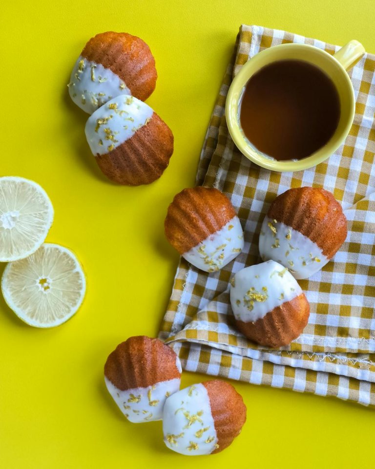 Top view of lemon-dipped madeleines and a cup of tea on a yellow background.