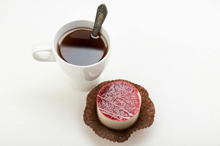 A delicious panna cotta with a raspberry glaze beside a cup of tea served with a spoon.