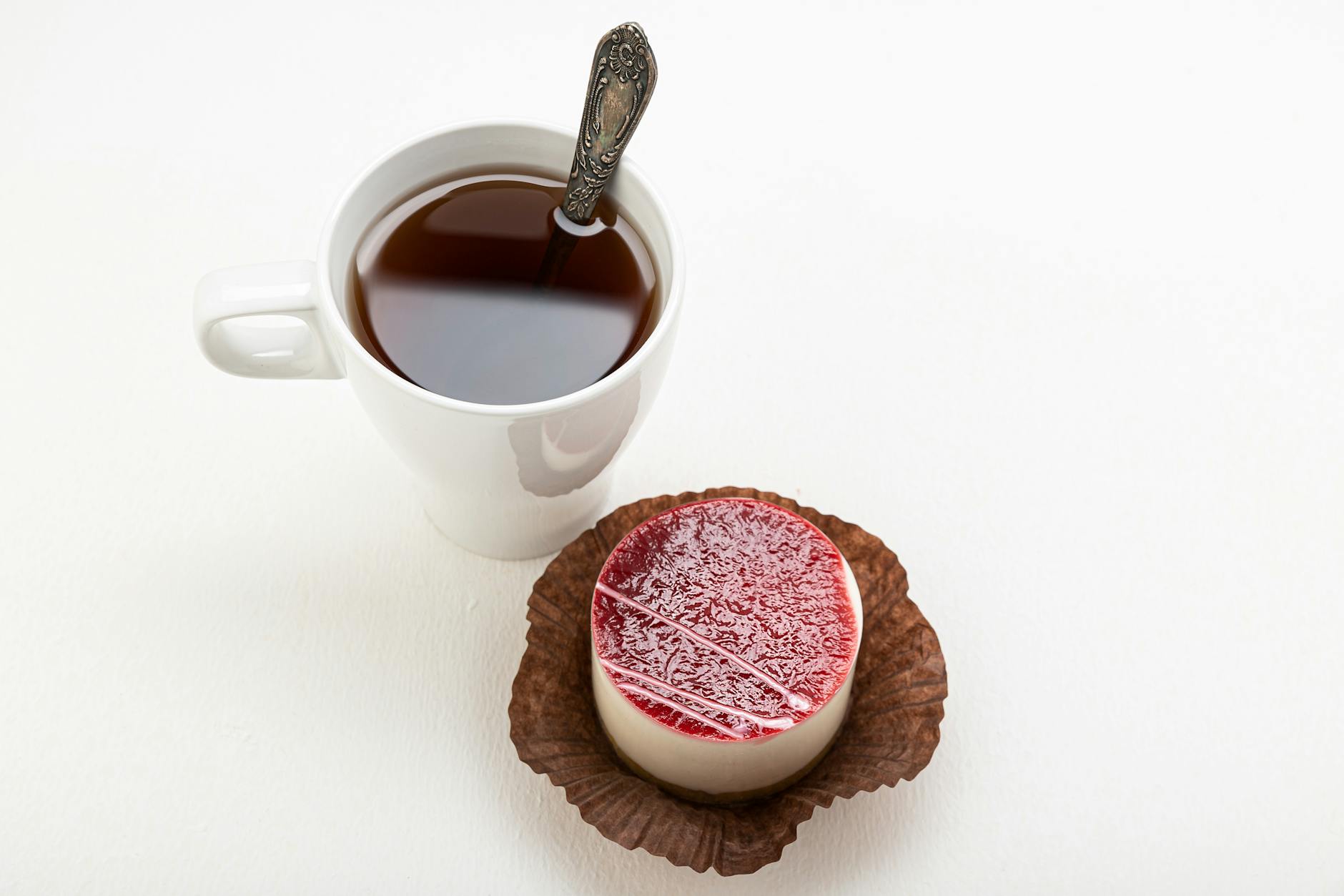 A delicious panna cotta with a raspberry glaze beside a cup of tea served with a spoon.