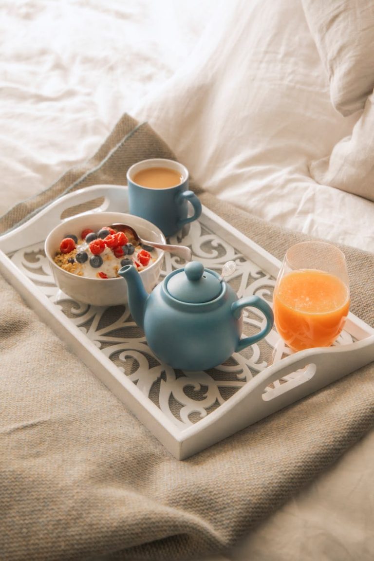 Inviting breakfast tray with tea, juice, and granola parfait on a bed linen.