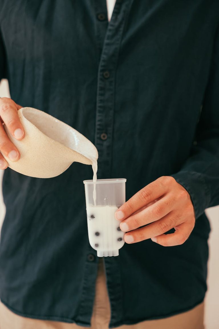 Close-up of hands pouring milk into a cup with tapioca pearls for bubble tea.