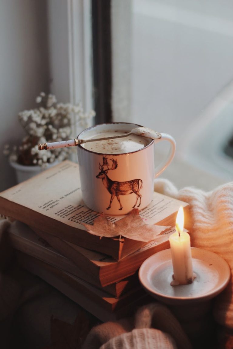 Warm autumn ambiance with a mug of coffee, candle, and books by a window.