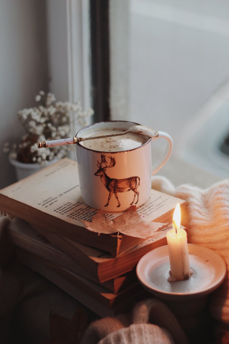 Warm autumn ambiance with a mug of coffee, candle, and books by a window.