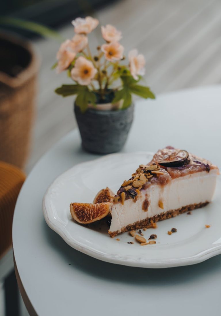 A slice of fig cheesecake garnished elegantly on a plate with flowers in the background.